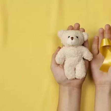 Fundo amarelo, um ursinho e o laço, símbolos da campanha de conscientização para a prevenção do câncer infantil